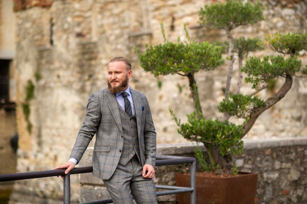 Ein Mann mit Bart in einem strengen grauen dreiteiligen Anzug mit Krawatte in der Altstadt von Sirmione, ein stilvoller Mann in einem grauen Anzug in Italien.