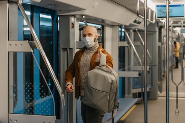 Ein Mann mit Bart in einer Gesichtsmaske, um die Ausbreitung des Coronavirus zu vermeiden, zieht einen Rucksack an, während er in einer U-Bahn fährt. Ein Glatzkopf mit Mundschutz hält in einem Zug soziale Distanz.