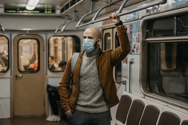 Ein Mann mit Bart in einer medizinischen Gesichtsmaske, um die Ausbreitung des Coronavirus zu vermeiden, hält sich in einem U-Bahn-Wagen am Handlauf fest. Ein Glatzkopf in einer OP-Maske gegen COVID-19 steht in einem U-Bahn-Zug.