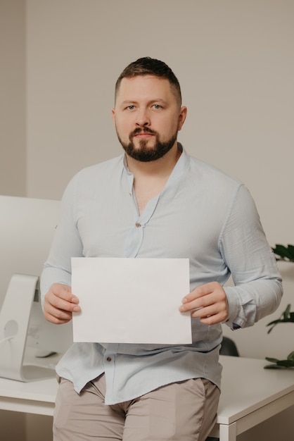 Ein Mann mit Bart sitzt mit einem leeren weißen Blatt Papier in der Nähe eines Desktop-Computers aus Stahl zu Hause