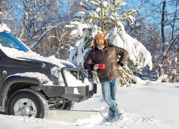 ein Mann mit Bart und Schnurrbart, der an einem sonnigen Tag in einem Winterwald eine Pelzmütze und eine Jacke trägt