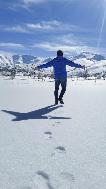 Ein Mann mit blauer Jacke, der die verschneite Natur umarmt und Freude hat und glücklich ist