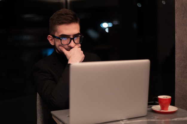 Ein Mann mit Brille sitzt an einem Tisch vor einem Laptop.