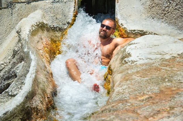Ein Mann mit Brille sitzt unter einem Wasserfall aus Heilwasser mit Thermalquellen in Pamukkale.Turkey.