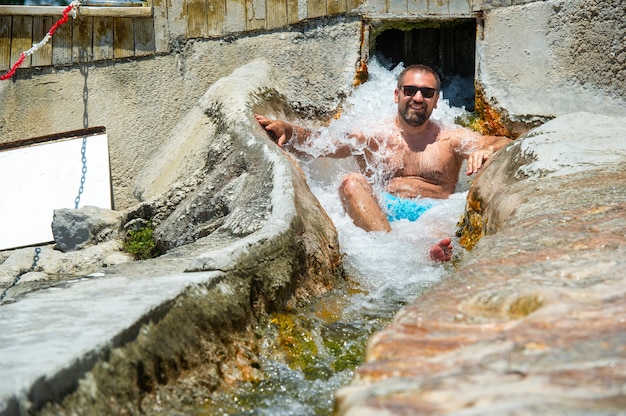 Ein Mann mit Brille sitzt unter einem Wasserfall aus Heilwasser mit Thermalquellen in Pamukkale.Turkey.