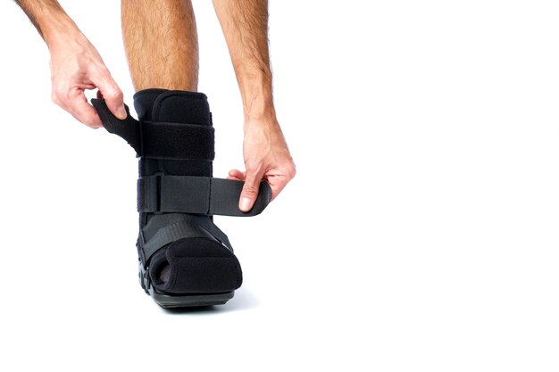 Ein Mann mit einem Bein von vorne, der einen orthopädischen Stiefel für Brüche und Verstaubungen auf weißem Hintergrund trägt