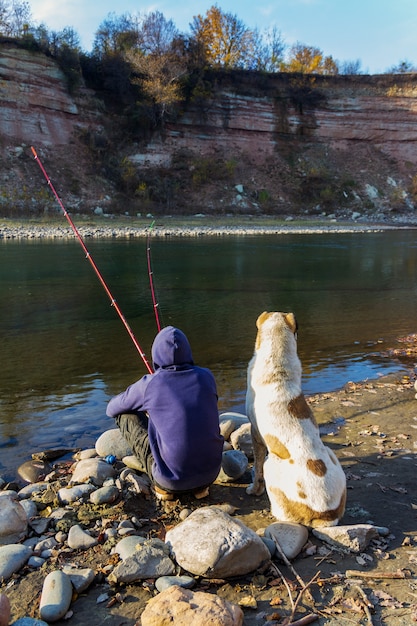 Ein Mann mit einem großen zentralasiatischen Schäferhund, der an einem Herbsttag im Fluss fischt