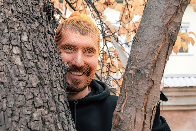 Ein Mann mit einem Messer in der Hand und einem Strumpf auf dem Kopf wartet hinter einem Baum auf sein Opfer