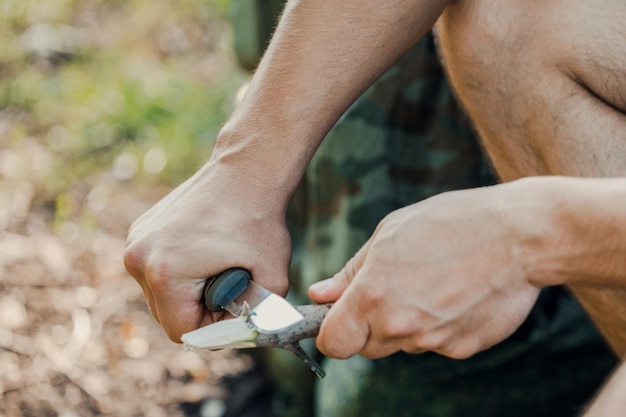 Ein Mann mit einem Messer schnitt einen Holzstab für ein Feuer im Wald