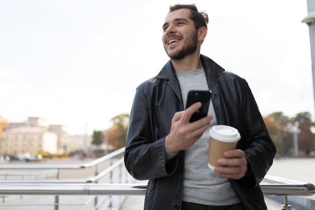 Ein Mann mit einem Mobiltelefon in der Stadt, der Kaffee trinkt