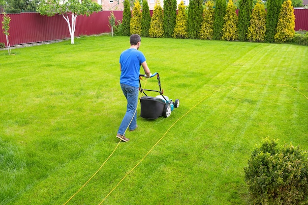 Ein Mann mit einem Rasenmäher schneidet grünes Gras, ein Gärtner, der im Hinterhof arbeitet