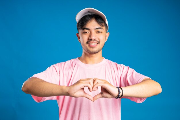 Foto ein mann mit einem rosa t-shirt und einem weißen hut hebt seine hände, um ein symbol der liebe zu bilden, der breit lächelt