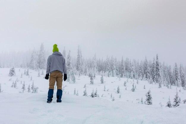 Ein Mann mit einem schönen Hut steht mit dem Rücken und beobachtet den Schneefall im Winterwald