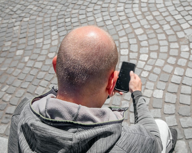 Ein Mann mit einem Smartphone in der Hand sitzt bei Tageslicht mitten in der Stadt