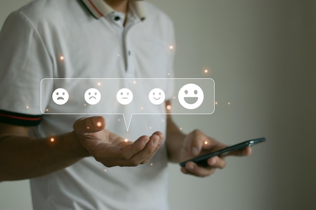 Ein Mann mit einem Smartphone wählt das Icon für ein glückliches Lächeln, um die Zufriedenheit mit dem Service zu zeigen. Sehr beeindruckende Ergebnisse über das drahtlose Netzwerk