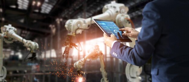 Ein Mann mit einem Tablet-Gerät, der in einer Fabrik von Roboterarmen umgeben ist