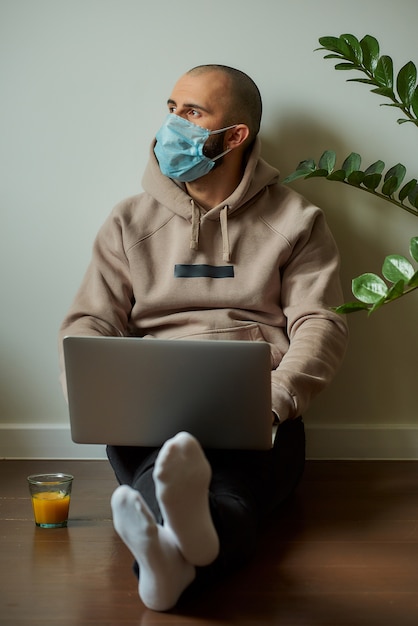 Ein Mann mit einer Gesichtsmaske, der an seinem Laptop arbeitet