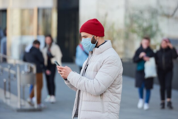 Ein Mann mit einer Gesichtsmaske im Gesicht mit einem Smartphone im Zentrum der Stadt.