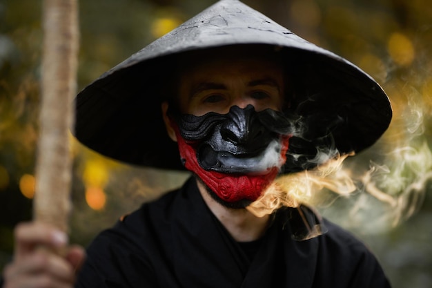 Ein Mann mit einer Hannya-Maske, einem schwarzen Kimono, einem schwarzen Hut mit einem Bambusstock in den Händen. Surrealer Samurai, Ninja