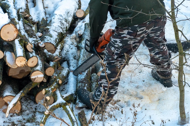 Ein Mann mit einer Kettensäge sägt Äste und Baumstämme Abholzung im Winter Die Arbeit eines Holzfällers bei strengen Winterbedingungen Fällen Sie alte Bäume in der Stadt