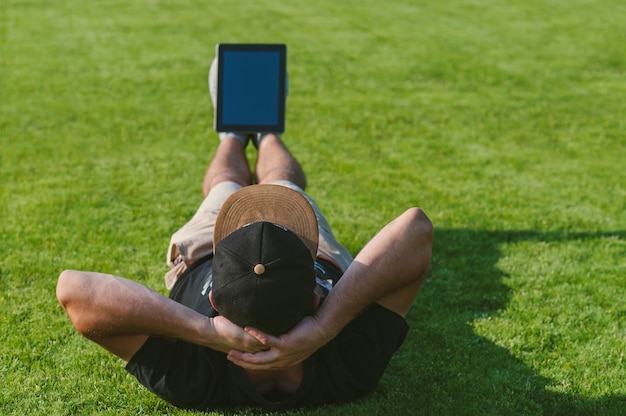 Ein Mann mit einer Tablette zu seinen Füßen macht Übungen. Auf der Wiese im Freien. Konzept zum Thema Online-Training.