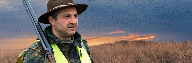 Ein Mann mit einer Waffe in der Hand und einer grünen Weste auf einer Fasanenjagd in einem Waldgebiet bei bewölktem Wetter Jäger mit Hunden auf der Suche nach Wild