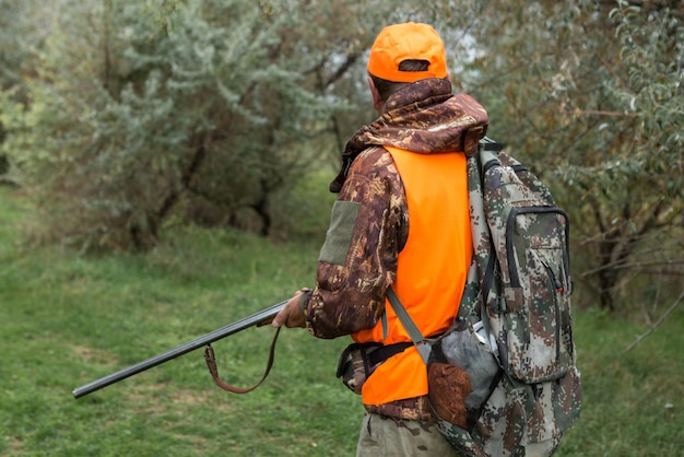 Ein Mann mit einer Waffe in der Hand und einer orangefarbenen Weste auf einer Fasanenjagd in einem Waldgebiet bei bewölktem Wetter Jäger mit Hunden auf der Suche nach Wild