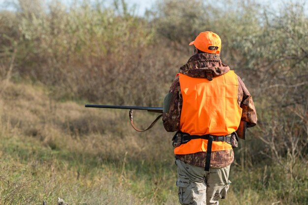 Ein Mann mit einer Waffe in der Hand und einer orangefarbenen Weste auf einer Fasanenjagd in einem Waldgebiet bei bewölktem Wetter Jäger mit Hunden auf der Suche nach Wild