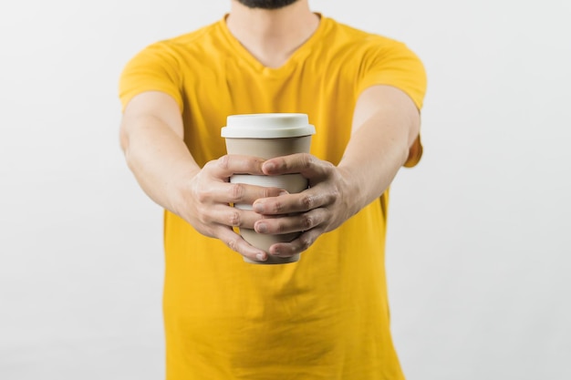 Ein Mann mit gelbem Hemd auf weißem Hintergrund bietet eine Kaffeetasse an