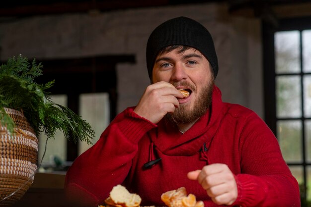 Ein Mann mit Hut und Pullover isst eine Mandarine