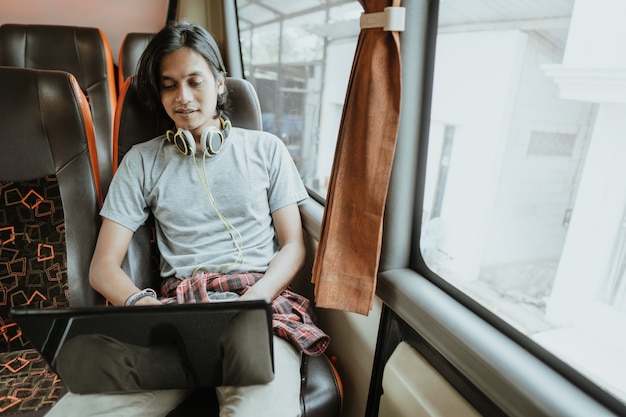 Ein Mann mit Kopfhörern benutzt einen Laptop, während er im Bus an einem Fenster sitzt