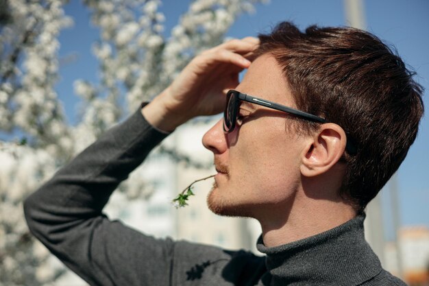 Ein Mann mit kurzen braunen Haaren und Sonnenbrille steht vor einem Baum mit weißen Blumen