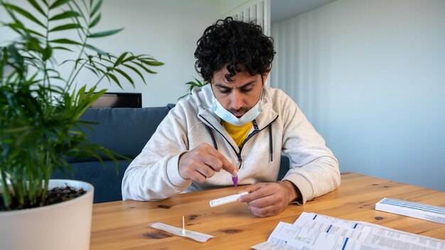 Ein Mann mit Maske, der die Probe zu Hause in das Kovid19-Antigen-Diagnosetestgerät einlegt Set mit Kassettenkit für Selbsttests zur Überprüfung der Infektion der Coronavirus-Quarantänepandemie