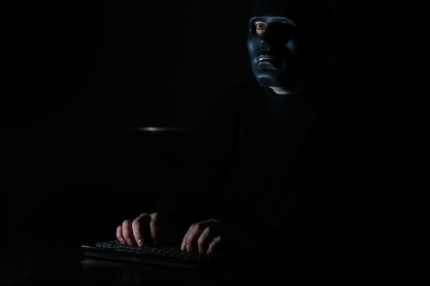 Ein Mann mit Maske druckt im Dunkeln auf der Tastatur