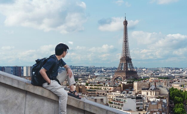 ein Mann mit Rucksack, der Eiffelturm, berühmtes Wahrzeichen und Reiseziel in Paris, Frankreich betrachtet