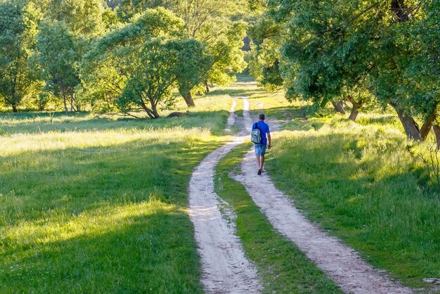 Ein Mann mit Rucksack geht auf einer unbefestigten Straße.