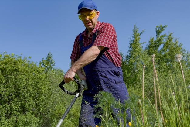 Ein Mann mit Schutzbrille mäht das Gras mit einem Rasenmäher Ein arbeitender Bauer Schneiden von Gras