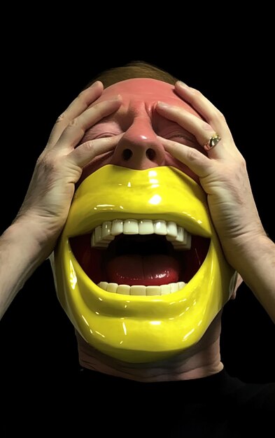 ein Mann mit seinen Händen auf seinem Gesicht und seinem Mund, der mit gelber Farbe bedeckt ist