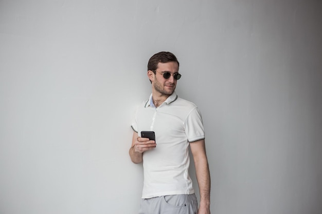 Ein Mann mit weißem T-Shirt und Brille hält ein Telefon in der Hand