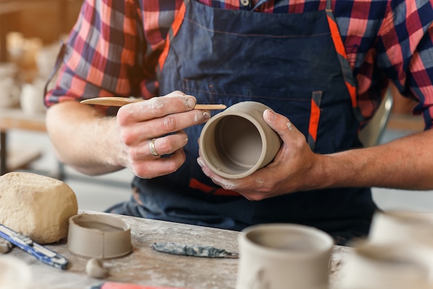 Ein Mann mittleren Alters in einer einheitlichen Arbeit von Holzstapel mit einer Tonform Tasse in einer großen kreativen Keramikmanufaktur.