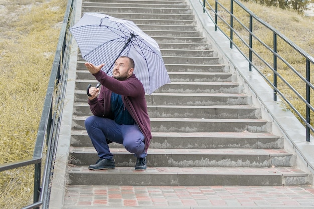 Ein Mann mittleren Alters mit Bart auf der Treppe unter einem Regenschirm