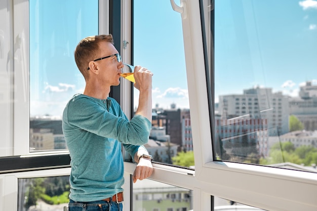 Ein Mann mittleren Alters steht auf dem Balkon eines Hochhauses und lehnt an den Fensterrahmen