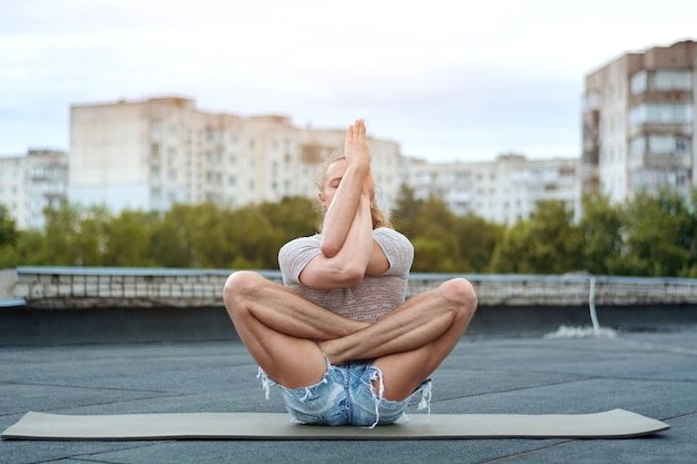 Ein Mann praktiziert Yoga auf dem Dach des Hauses. Yoga bei Sonnenuntergang. Gesundes Leben, Sport und Meditationskonzept.