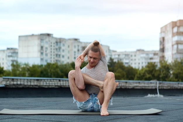 Ein Mann praktiziert Yoga auf dem Dach des Hauses. Yoga bei Sonnenuntergang. Gesundes Leben, Sport und Meditationskonzept.