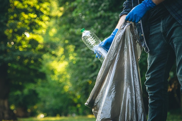 Ein Mann räumt den Wald auf und wirft eine Flasche in einen Müllsack