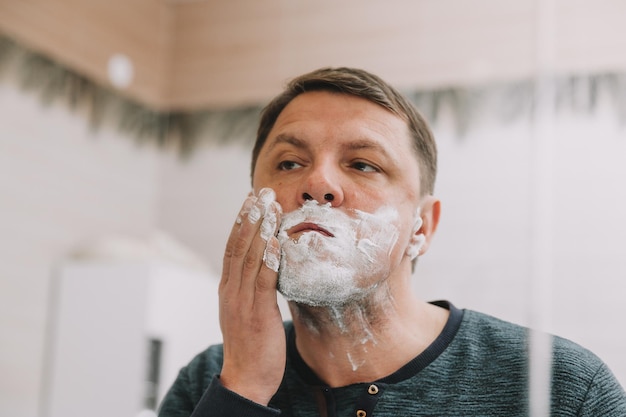 Ein Mann rasiert seinen Bart vor einem Spiegel in seinem Badezimmer.