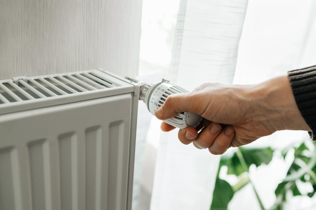 Ein Mann regelt die Temperatur am Heizkörper zu Hause steigende Heizpreise in den Haushalten