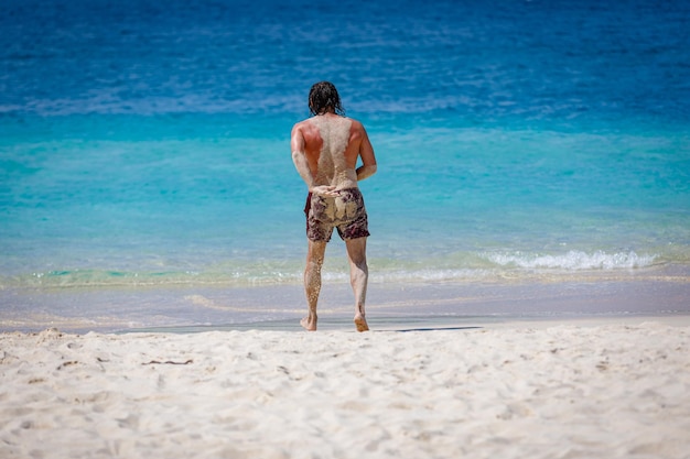 Ein Mann rennt, um im blauen Meer zu schwimmen. Der Rücken des Körpers ist mit Sand bedeckt.