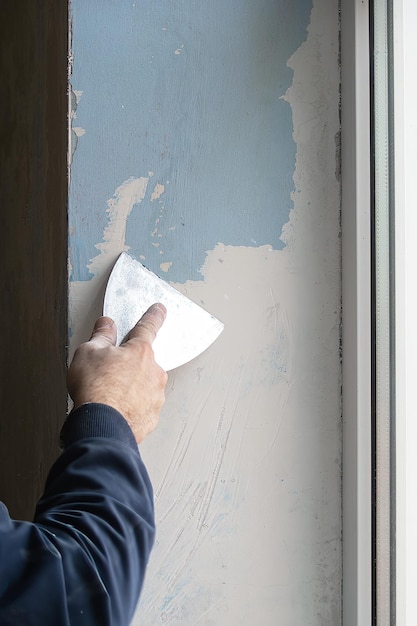 ein mann repariert zu hause, in seinen händen einen spachtel, mit dem er alte farbe von den wänden reinigt