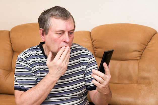 Ein Mann schaut emotional in ein Smartphone, während er auf der Couch sitzt